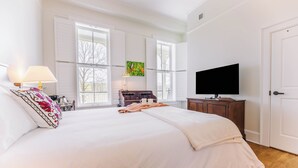 A bedroom with a large bed, a television, a desk with a lamp, and a window with a butterfly painting. - First-Floor Queen Room with Mountain Views (Max Meadows)