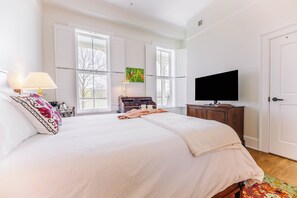 A bedroom with a large bed, a television, a desk with a lamp, and a window with a butterfly painting. - First-Floor Queen Room with Mountain Views (Max Meadows)