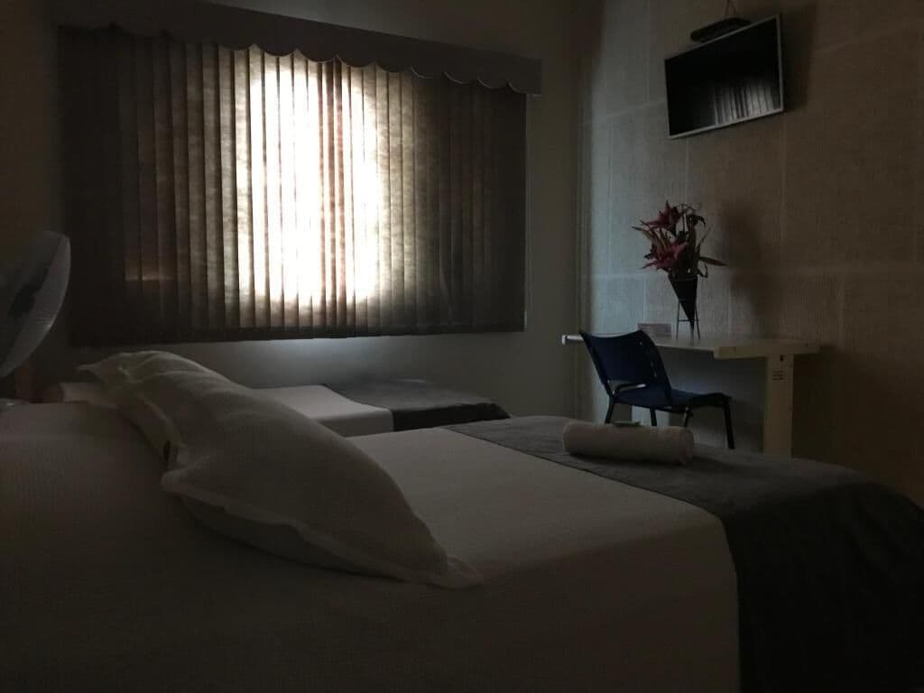Una habitación de hotel con cama, una silla, un escritorio y un ventanal con cortinas.