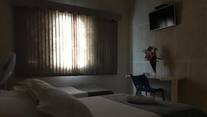 Ein Hotelzimmer mit einem Bett, einem Sessel, einem Schreibtisch und einem Fenster mit Vorhängen.