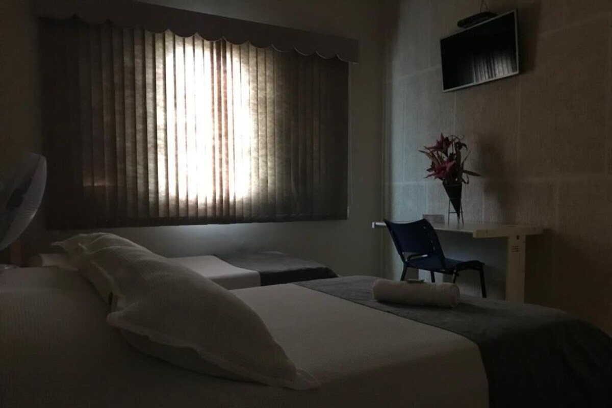 A hotel room with a bed, a chair, a desk, and a window with curtains.