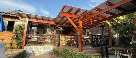 Un espacio exterior cubierto con una pérgola de madera, un edificio de ladrillo y un patio con baldosas.