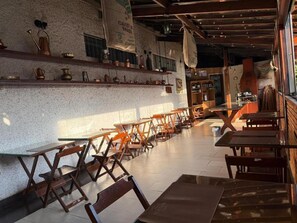 A café interior with wooden tables and chairs, a tiled floor, and shelves with kitchenware. - Hotel Arlen 3 Pousada Castelo (Careaçu)