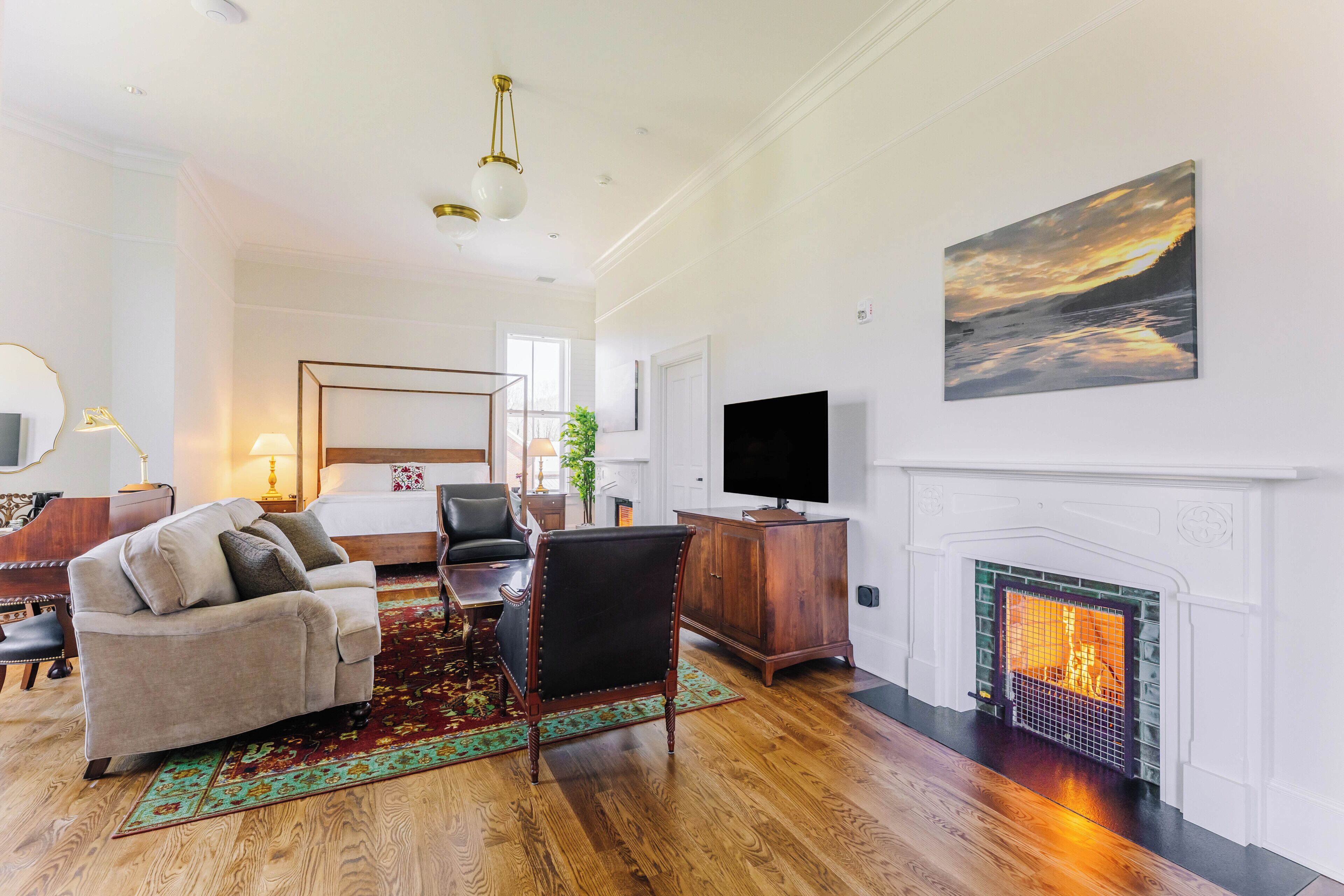 A hotel room with a bed, a TV, a fireplace, and a painting.