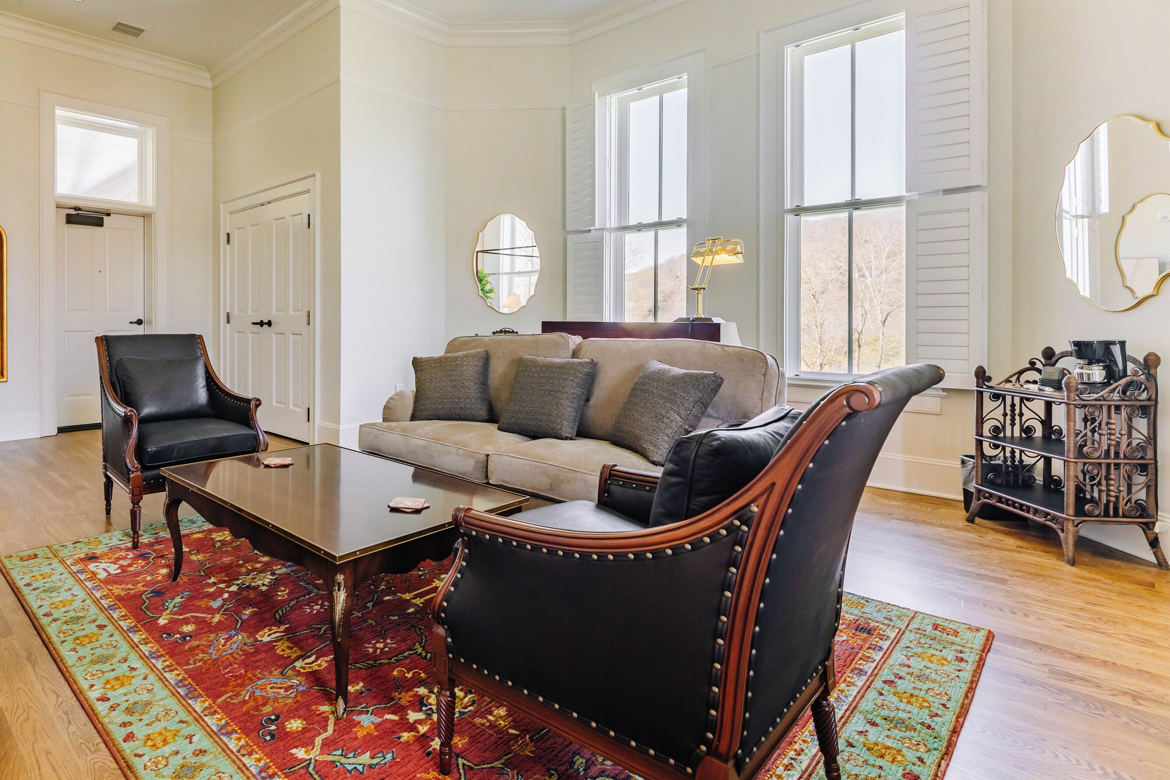 Un salon avec un canapé beige, deux fauteuils en cuir noir, une table basse en bois et un tapis à motifs.