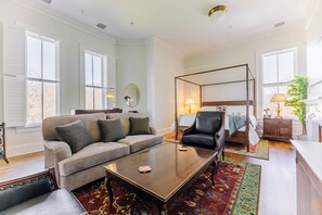 A spacious living room with a large sofa, a coffee table, and a four-poster bed. - Historic Honeymoon King Suite by New River Trail (Max Meadows)