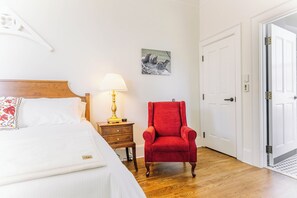 A hotel room with a bed, a red armchair, a bedside table with a lamp, a picture on the wall, and a door. - Large Historic King Room by New River Trail (Max Meadows)