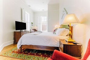 A hotel room with a bed, a television, a desk with a lamp, a chair, and a window. - Large Historic King Room by New River Trail (Max Meadows)