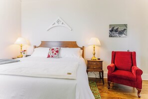 A neatly made bed with white linens, a red floral pillow, and two bedside lamps.