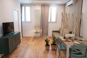 Ein modernes Wohnzimmer mit Fernseher, Sofa, Esstisch und Topfpflanzen.