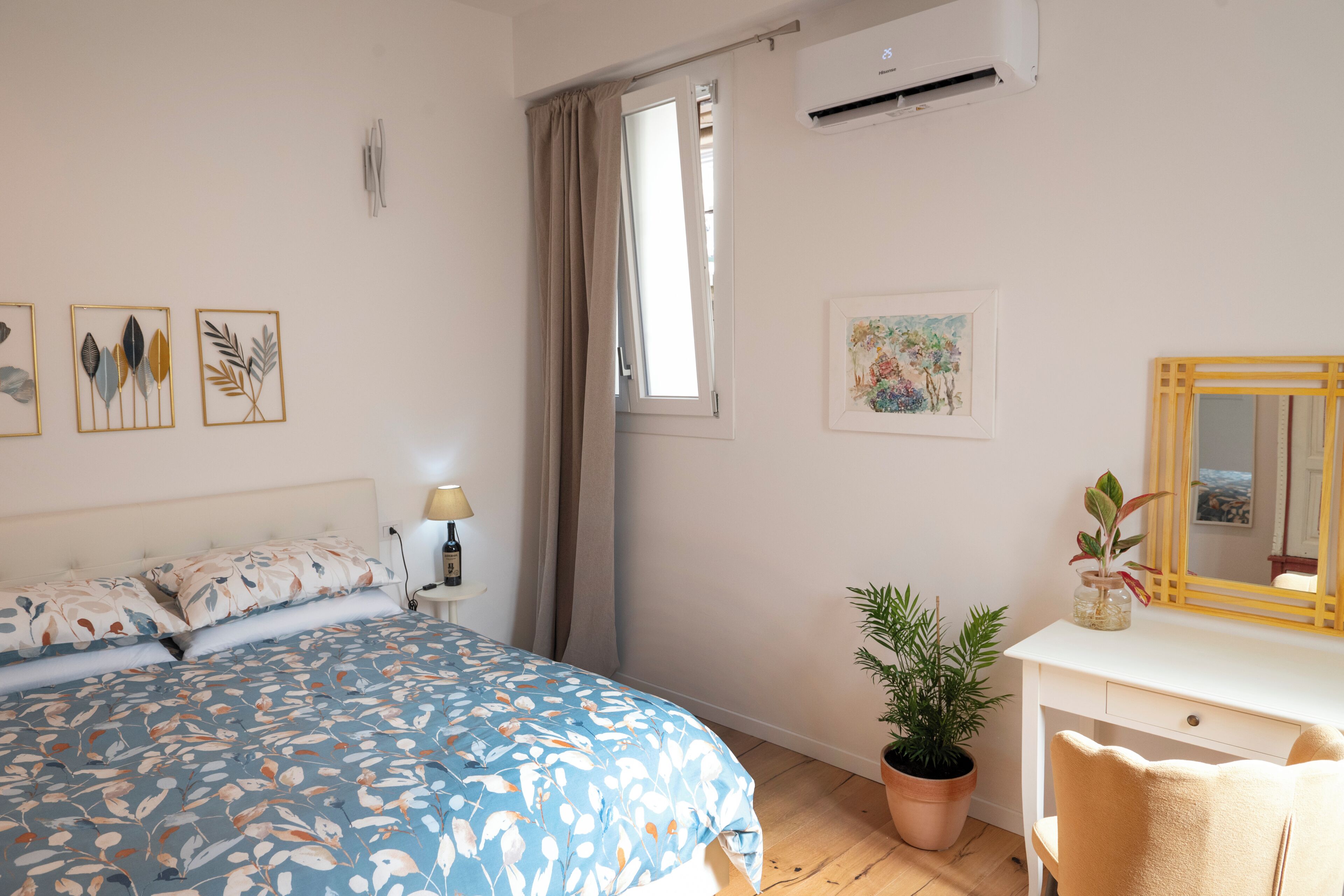 Een slaapkamer met een bed, een bureau met een spiegel, een potplant en kunst aan de muren.