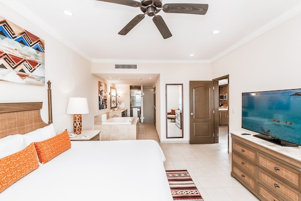 A hotel room with a bed, a television, a ceiling fan, and a view of the kitchen.
