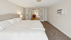 Ett hotellrum med en stor säng, en dörr som leder ut till en korridor och en väggmonterad luftkonditioneringsanläggning.