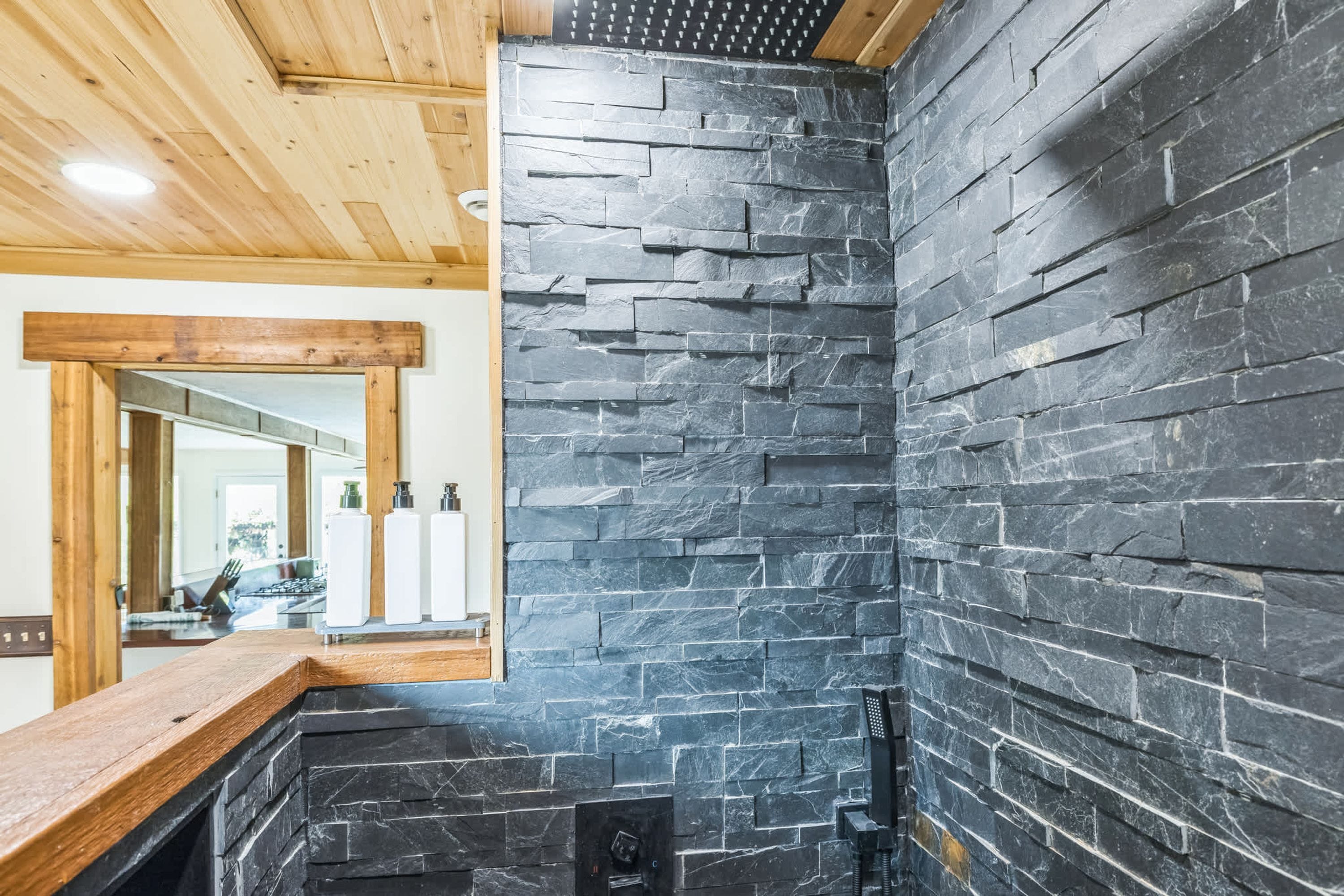 A bathroom with a stone wall, wooden ceiling, and a mirror.