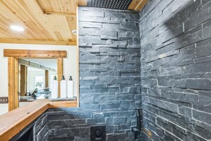 A bathroom with a stone wall, wooden ceiling, and a mirror. - 5-acre Historic Home With Pool Fishing Pond Game Room Outdoor Bar (Augusta)