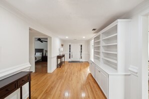 A hallway with wooden flooring, white walls, and a built-in shelving unit on the right. - 5-acre Historic Home With Pool Fishing Pond Game Room Outdoor Bar (Augusta)