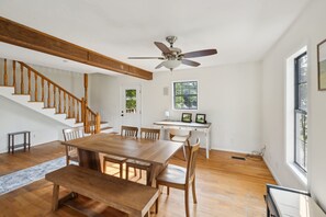 A spacious room with a wooden staircase, a dining table with chairs, a ceiling fan, and a window with a view of trees. - 5-acre Historic Home With Pool Fishing Pond Game Room Outdoor Bar (Augusta)