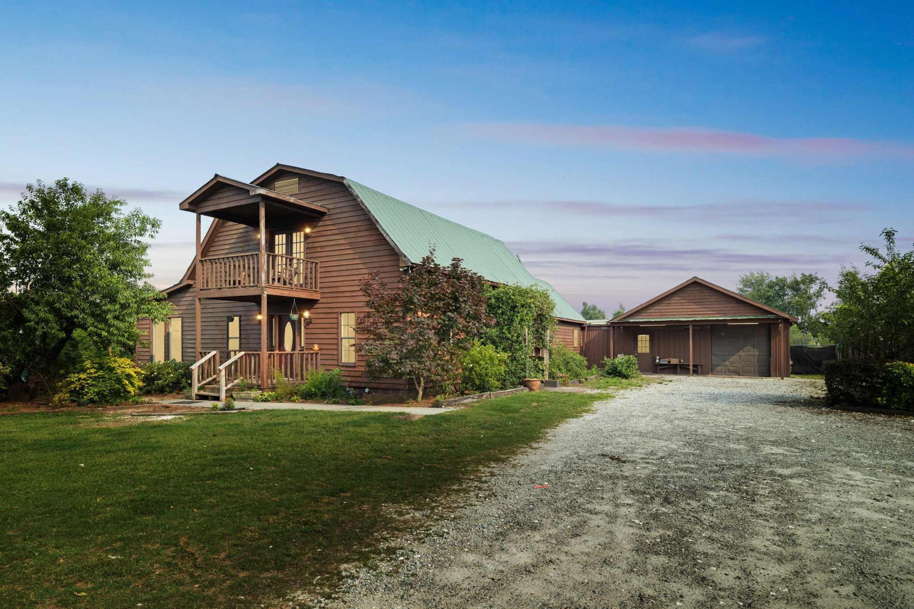 A two-story wooden house with a balcony, a garage, and a gravel driveway.