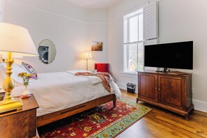 Een slaapkamer met een bed, bedlampen, een televisie, een houten kast en een raam.