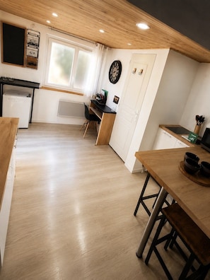 A modern kitchen with wooden flooring, a dining area with a wooden table and chairs, a refrigerator, and a window with curtains.