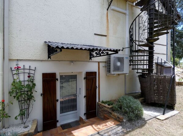 A residential building with a white exterior, a metal staircase, a small garden area with plants, and a door with a metal gate. - 7min Futuroscope - Havre de paix familial (Jaunay-Clan)