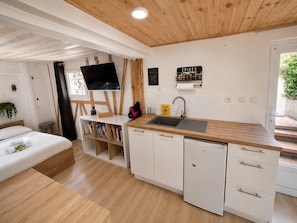 A compact kitchenette with a sink, a small refrigerator, and a flat-screen TV mounted on the wall.