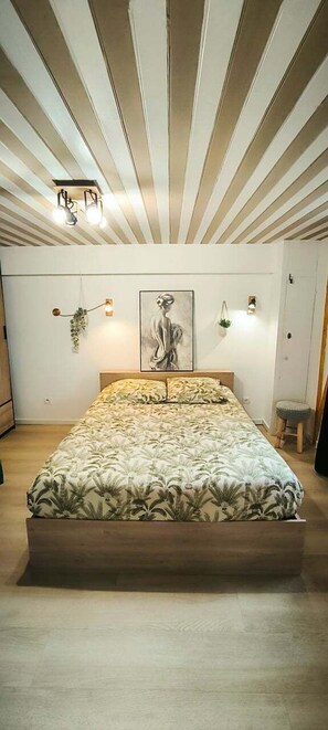 A bedroom with a large bed, a wooden headboard, a wall-mounted light fixture, and a framed artwork above the bed. - 7min Futuroscope - Havre de paix familial (Jaunay-Clan)