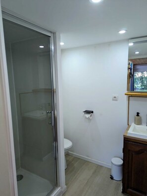 A bathroom with a glass shower enclosure, a toilet, a sink, and a trash bin. - 7min Futuroscope - Havre de paix familial (Jaunay-Clan)