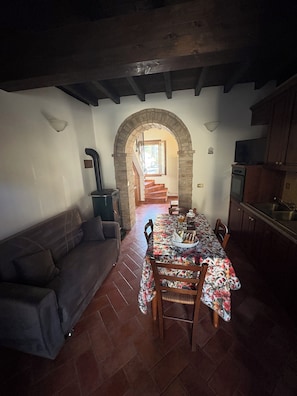 A dining area with a table set for four, a sofa, and a kitchen with a stove and sink.