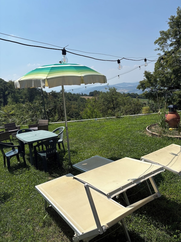 An outdoor seating area with a table and chairs, a green and white umbrella, and a view of the landscape.