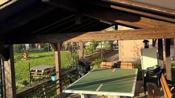 En uteplats med ett bord och stolar, en pergola som ger skugga och utsikt över en trädgård.