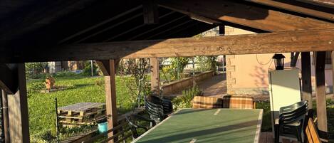 Un área de patio al aire libre con mesa y sillas, una pérgola arriba y vista a un jardín.