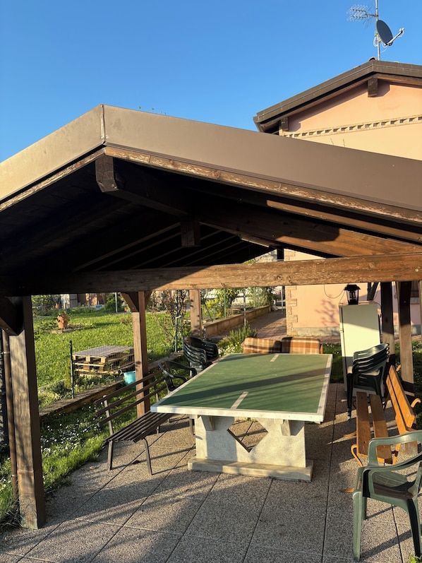 An outdoor patio area with a table and chairs, a pergola overhead, and a view of a garden.