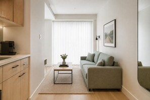 Ein stilvolles Wohnzimmer mit einer Couch, einer Kaffeemaschine, einem kleinen Tisch mit einer Vase und einem Fenster mit Jalousien.