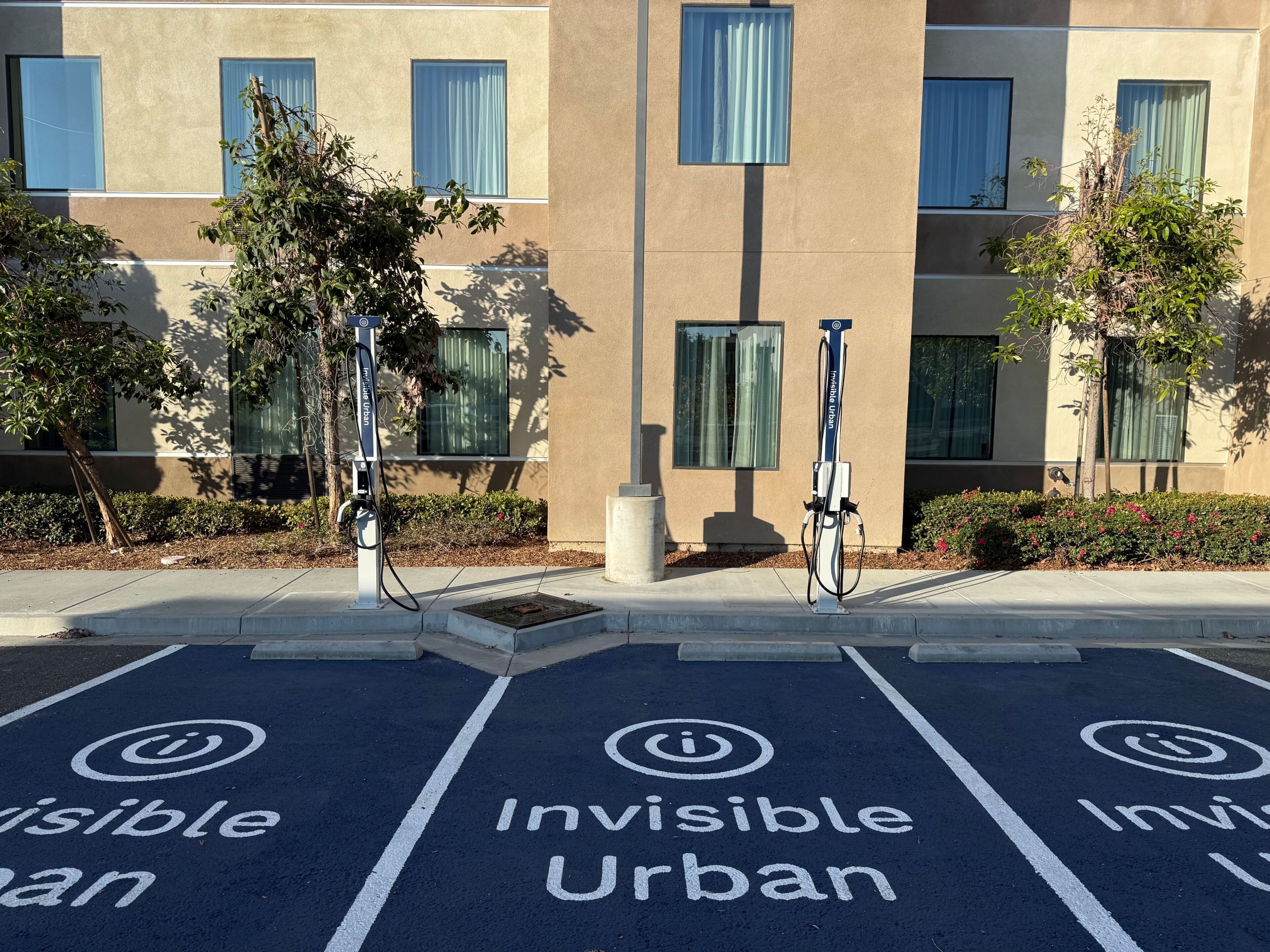 A parking area with electric vehicle charging stations and 'Invisible Urban' painted on the ground.