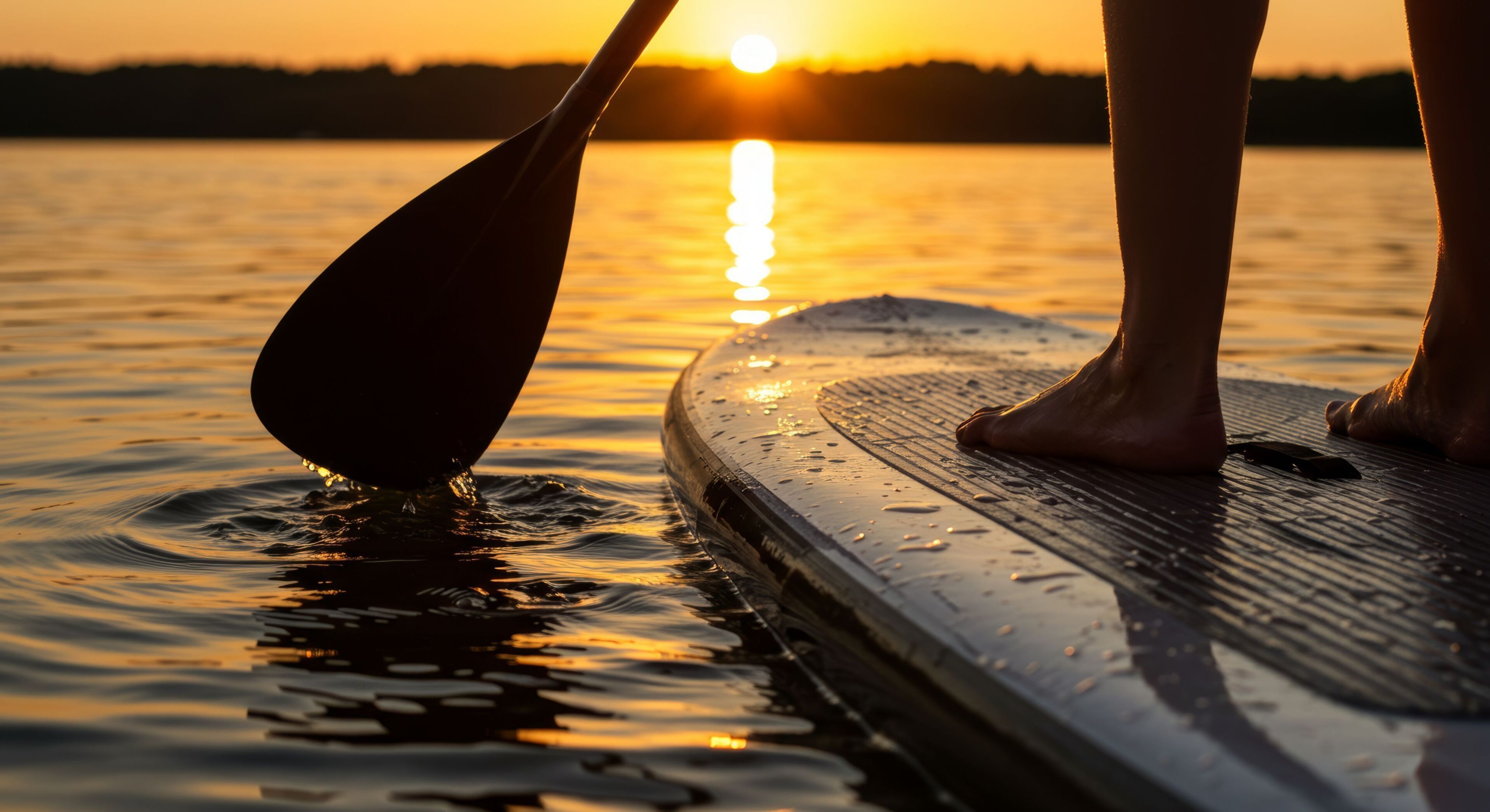 A person standing on a paddleboard with a sunset in the background.