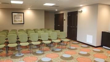A conference room with rows of green chairs, a patterned carpet, and a framed picture on the wall.