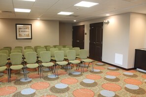 A conference room with rows of green chairs, a patterned carpet, and a framed picture on the wall.