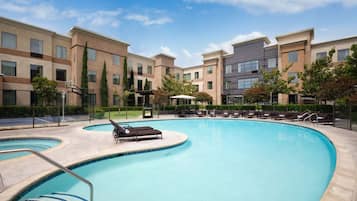 A swimming pool with lounge chairs and a basketball court, surrounded by multi-story buildings.