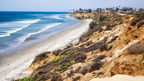 Eine Küstenlandschaft mit Sandstrand, felsigen Klippen und einer entfernten Wohngegend.