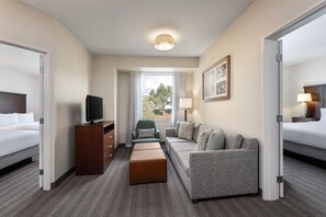 A hotel room with a bed, a sofa, a TV, a desk, and a window with a view of trees.