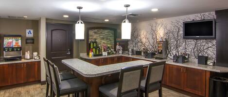 A kitchen with a bar area, wooden cabinets, and a television mounted on the wall.