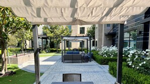 An outdoor patio area with a covered seating area, a table with chairs, and a garden with white flowers. - ADA Suite w/ Roll-in Shower | Free Breakfast (Carlsbad)