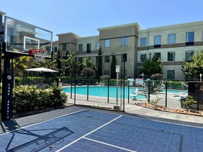 A pool area with a basketball court, a fence, and a building with a sign. - ADA Suite w/ Roll-in Shower | Free Breakfast (Carlsbad)