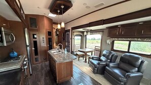Una cocina con una isla central, un comedor con mesa y sillas, y una sala de estar con sofás de cuero.
