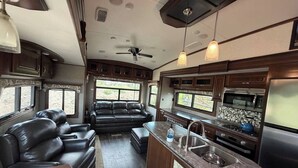 A compact RV interior with a kitchenette, seating area, and a ceiling fan. - Bozeman Basecamp | Luxury RV 11 min from BZN (Belgrade)