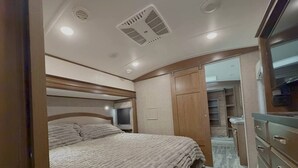 A bedroom with a bed, a dresser, a television, and a closet. - Bozeman Basecamp | Luxury RV 11 min from BZN (Belgrade)