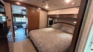 A bedroom with a bed, a headboard, and a window. - Bozeman Basecamp | Luxury RV 11 min from BZN (Belgrade)