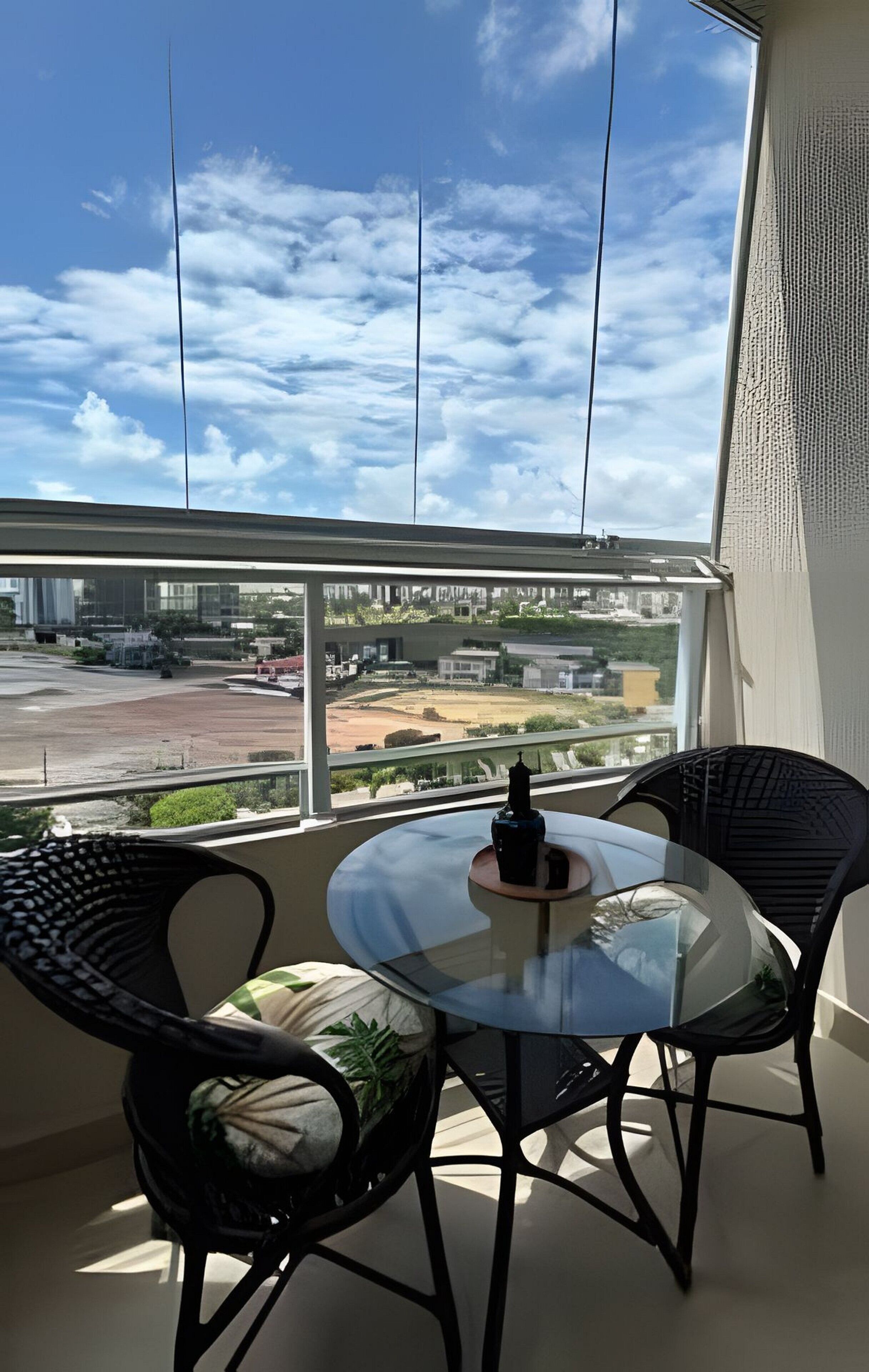 Ein modernes Zimmer mit einem Glastisch und Stühlen, Blick auf eine Stadtkulisse durch große Fenster und einem klaren Himmel.