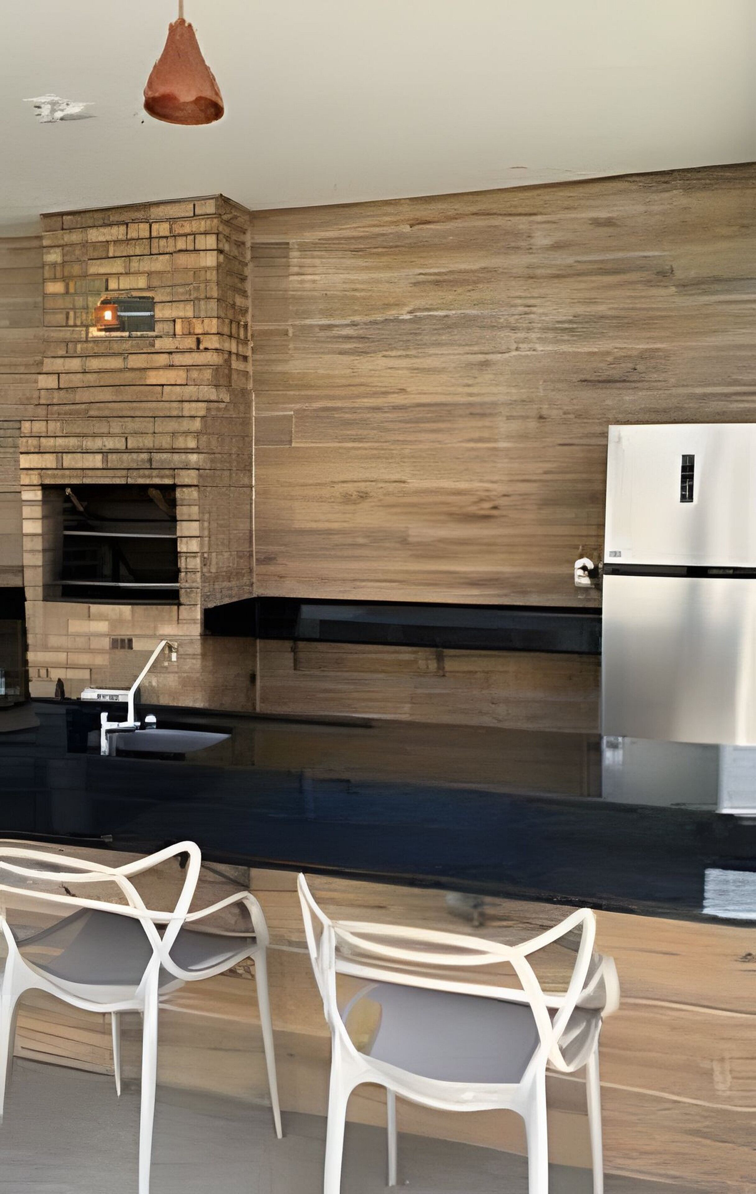 A modern kitchen with a brick fireplace, a stainless steel refrigerator, and two white chairs.
